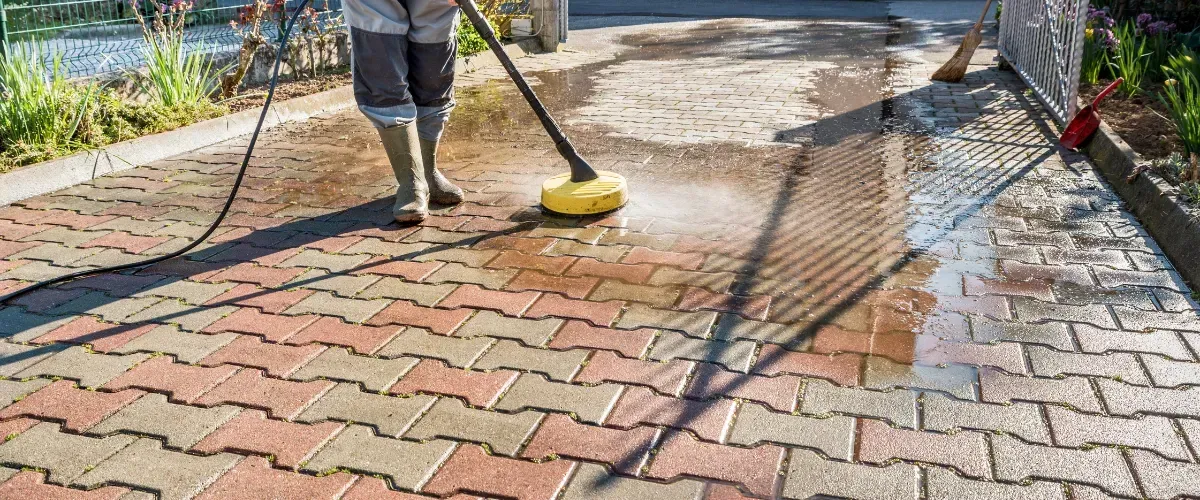 Worker pressure washing a brick driveway, showing dramatic before and after results.