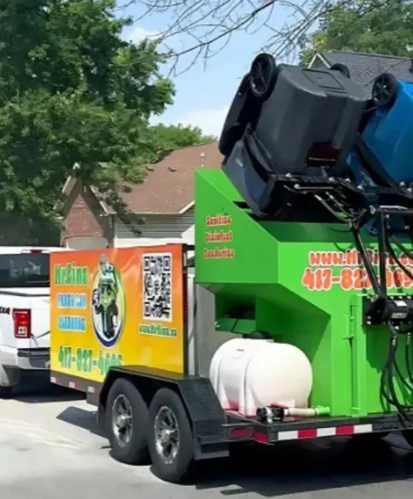 Mr. Binz trash bin cleaning trailer in action with bins lifted for cleaning.