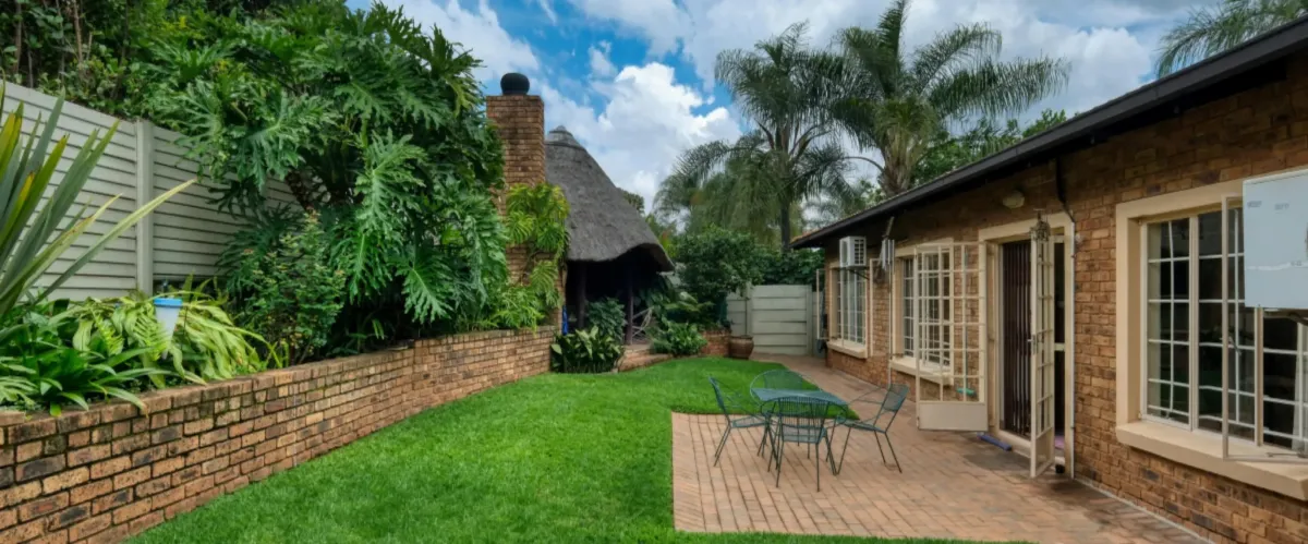 Tropical backyard patio with brick house, palm trees, and landscaped garden.