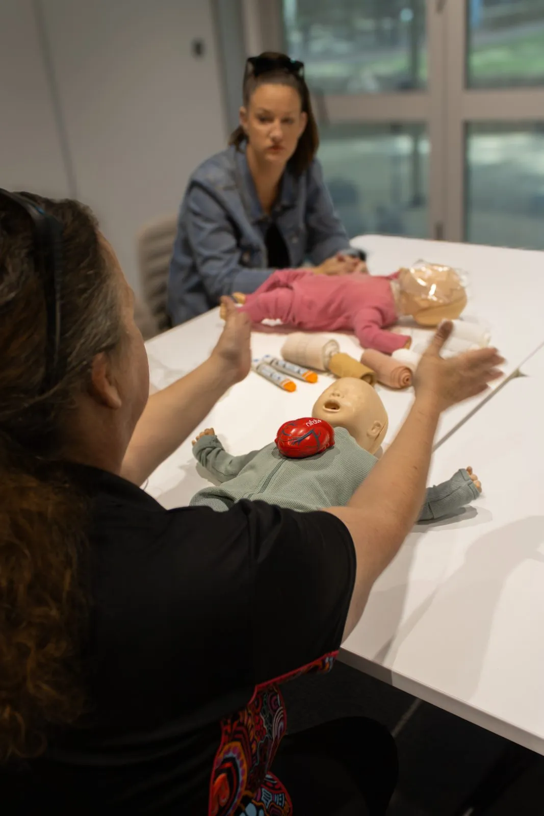 Britt explaining a first aid scenario to a participant at a table with training manikins