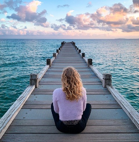 A woman sitting peacefully on a wooden boardwalk stretching toward the horizon, symbolizing mental clarity and the journey toward gut-brain balance at ColonCARE Mauritius.