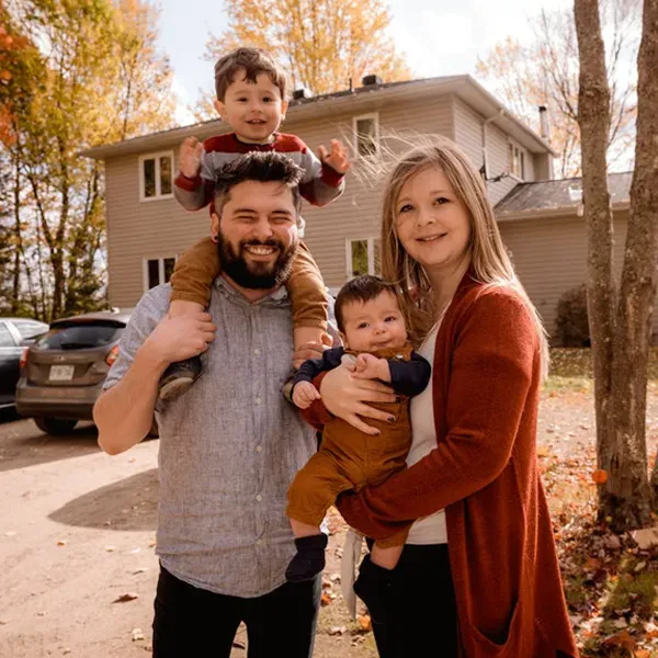family posing and smiling for the camera infront of their home in the autumn