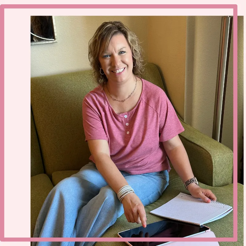 Christian mom sitting on a couch using a tablet and notebook to plan her evening routine for a calm, organized home and business. 
