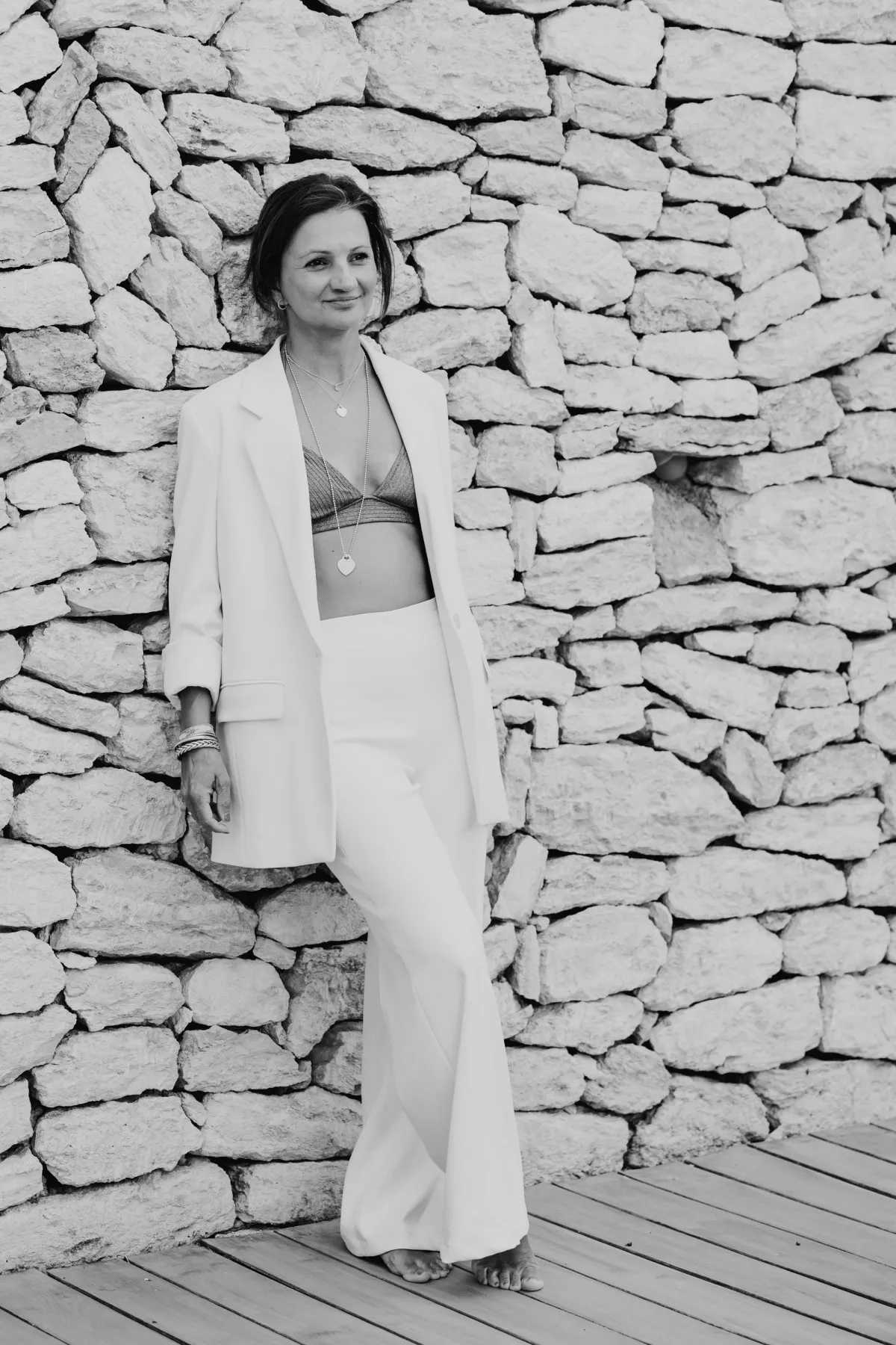 Personal Branding Porträt in Schwarz-Weiß: Selbstbewusste Unternehmerin im weißen Anzug vor einer rustikalen Steinmauer