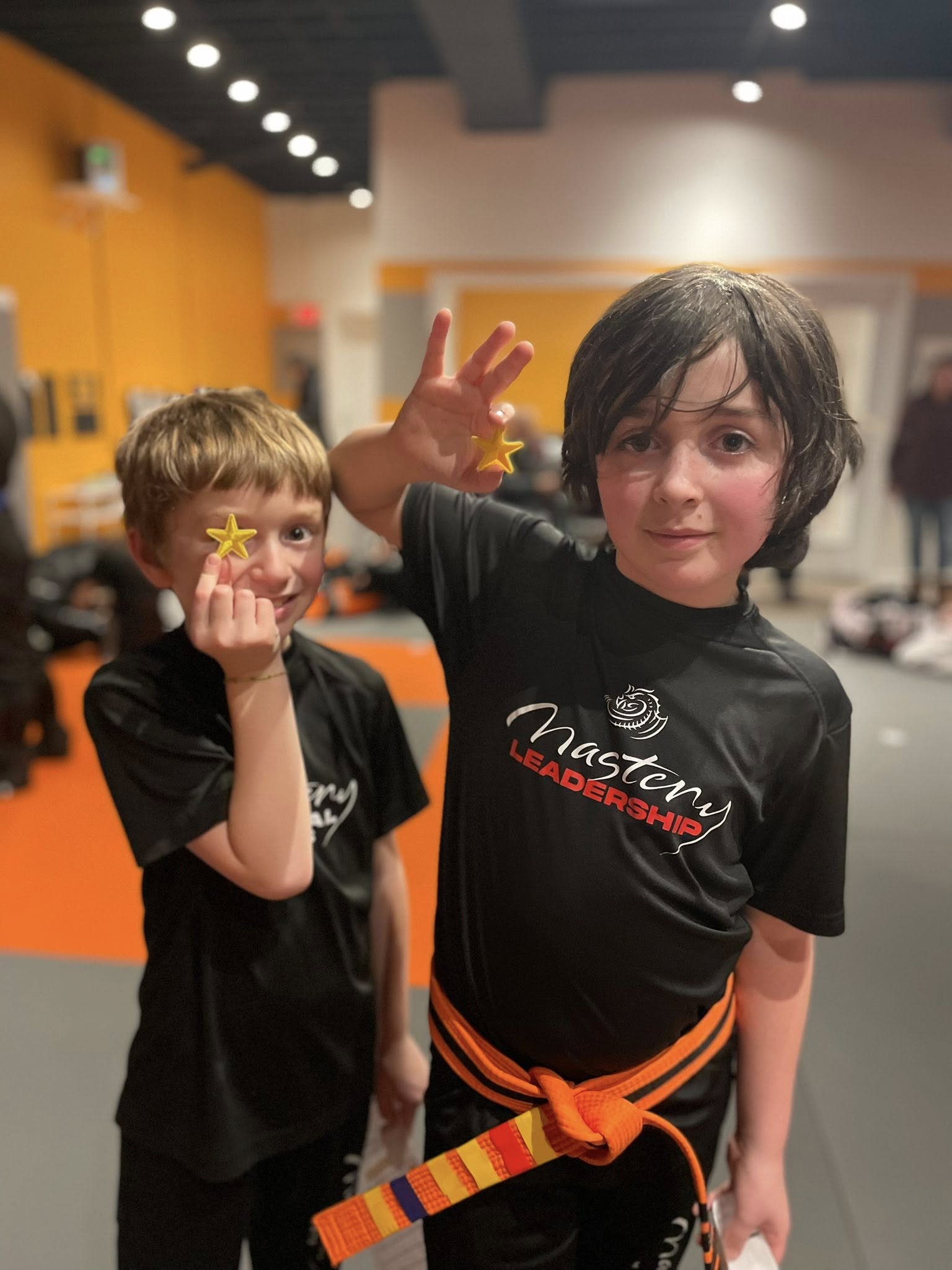 Two Mastery Martial Arts students holding achievement stars in a supportive training environment, representing how positive reinforcement builds confidence instead of fear-based discipline.