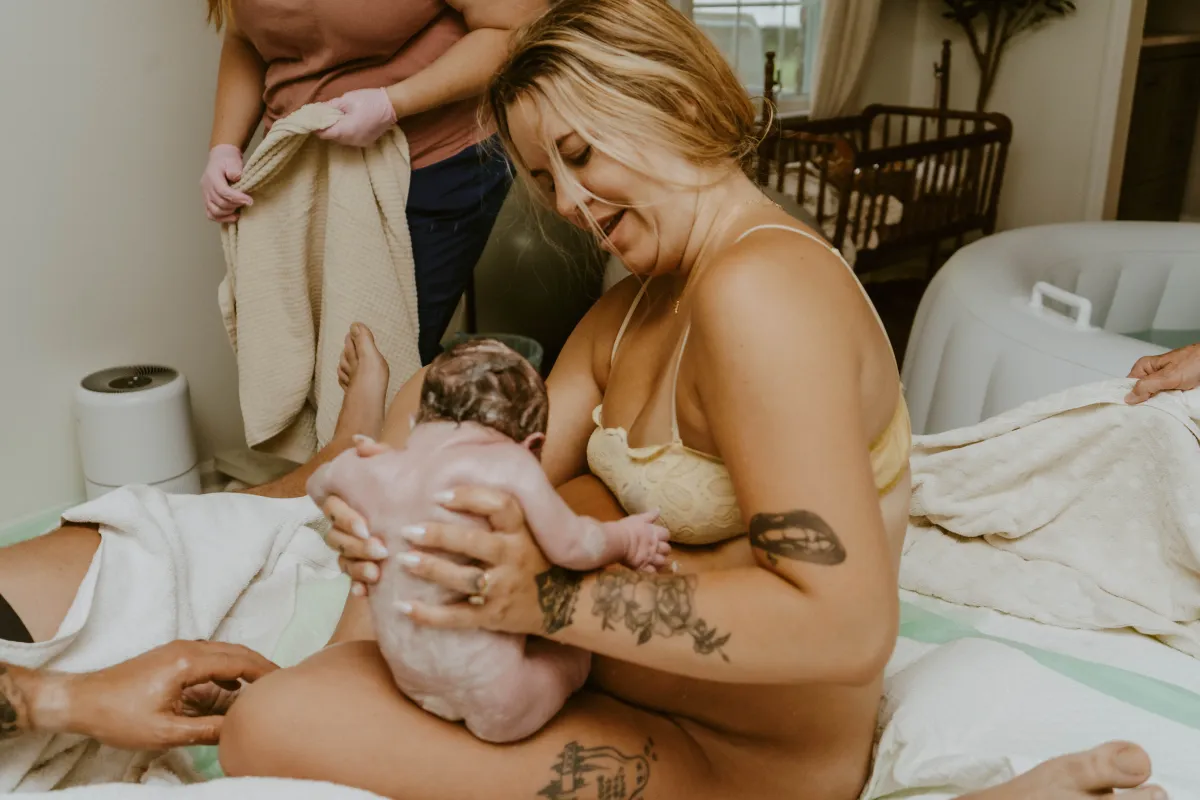 Mother holding her newborn with support after home birth