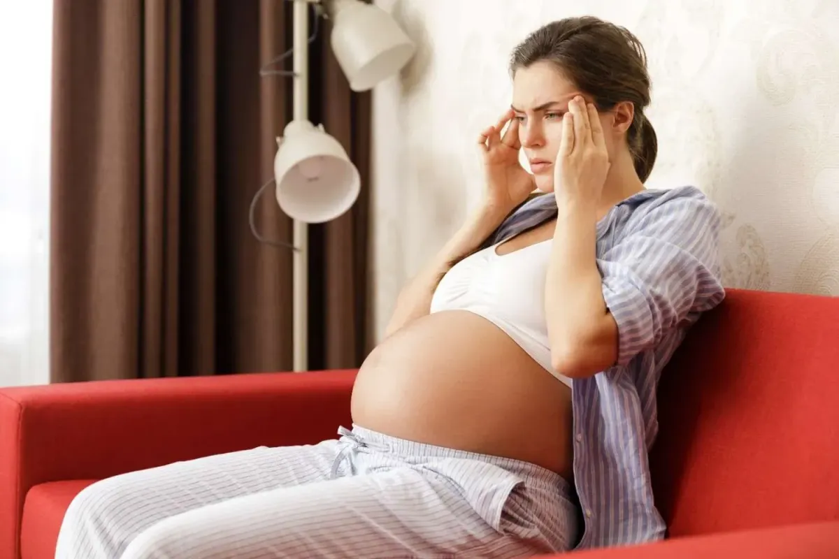 Pregnant woman experiencing stress and discomfort while sitting at home during pregnancy
