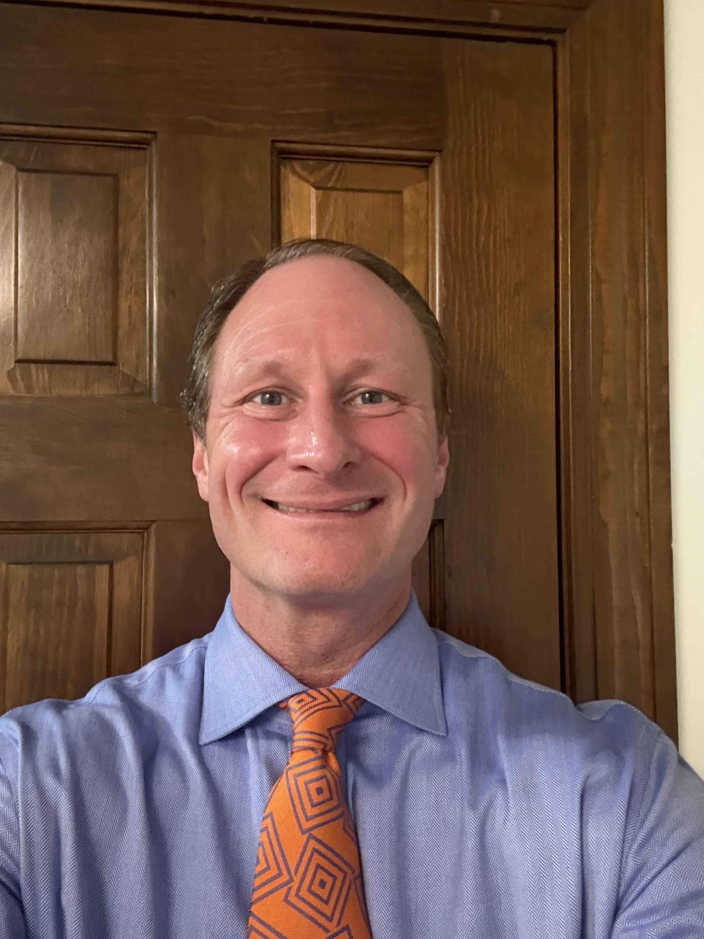 Merritt Wagoner at a courtroom table, reviewing documents with focused attention. The setting is a sunlit, classic courtroom with wood paneling. The image is 3:2, showing professionalism and dedication, with a subtle gold accent in a tie clip.