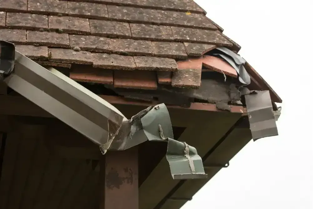 Storm-damaged roof with broken shingles and gutter in Georgetown, TX before emergency repairs