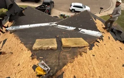 Roof replacement in progress with exposed decking and workers preparing for new shingles.