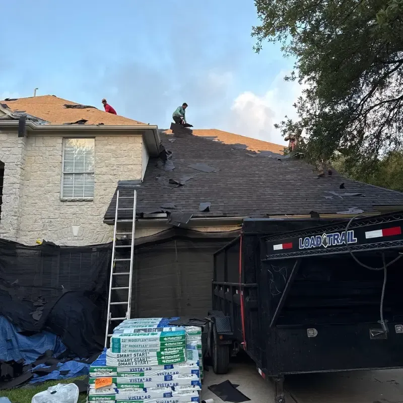 Roof tear-off in progress on a two-story home with workers removing old shingles and materials.