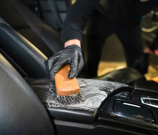 A man brushing the car seat, detailing the interior with a cleaning brush