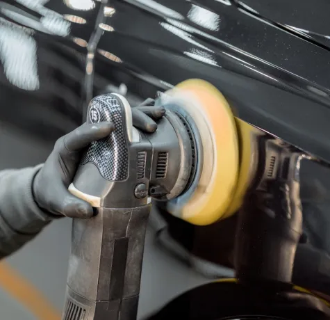 A hand polishing the surface of a car with a polishing machine.