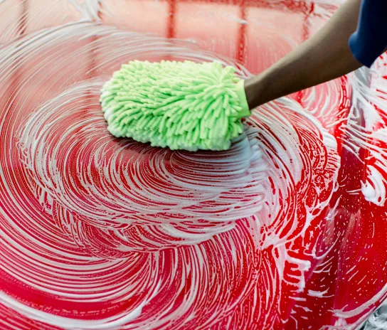 a hand cleaning a red car using a cloth