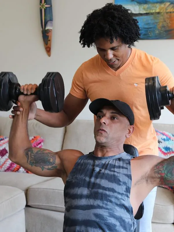 Coach Junior guiding a client through dumbbell shoulder press during an in-home personal training session.