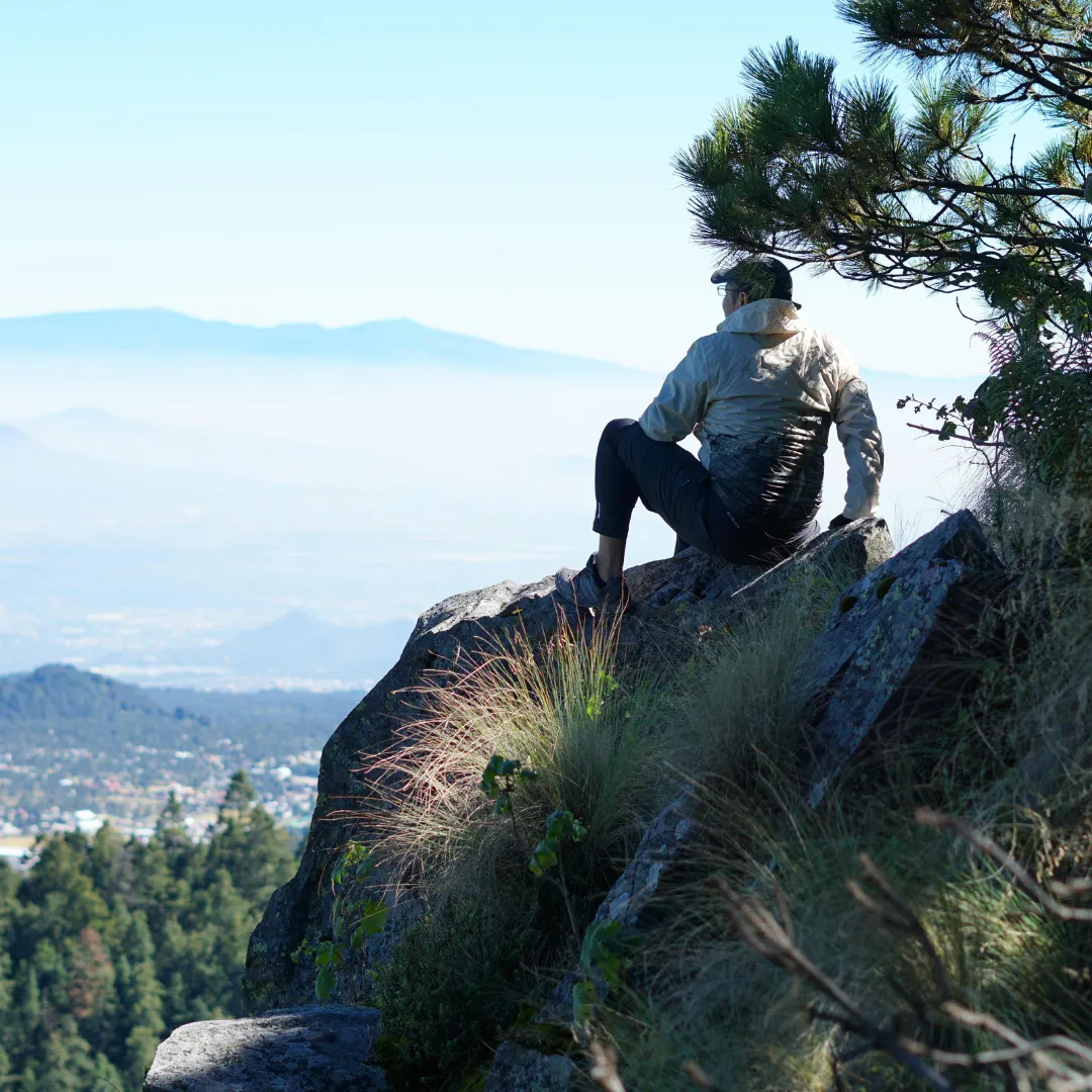 Person sitting on a mountain rock overlooking a scenic valley representing the health transformation and wellness journey at Solutions Functional Medicine Centre