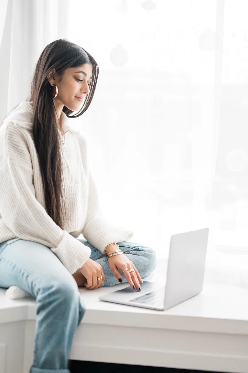 Amber Farooqui working on her laptop by a window