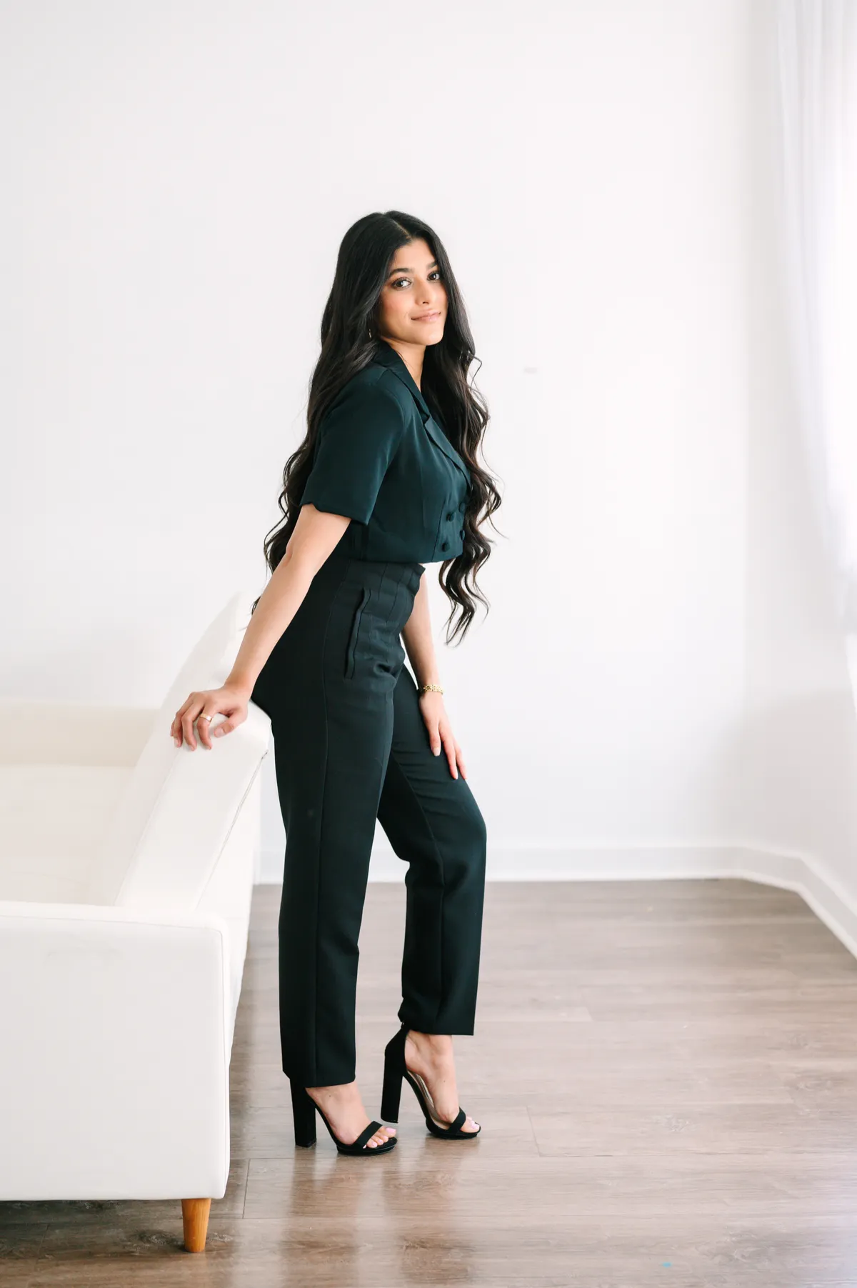 Amber Farooqui in a dark green outfit beside a white chair