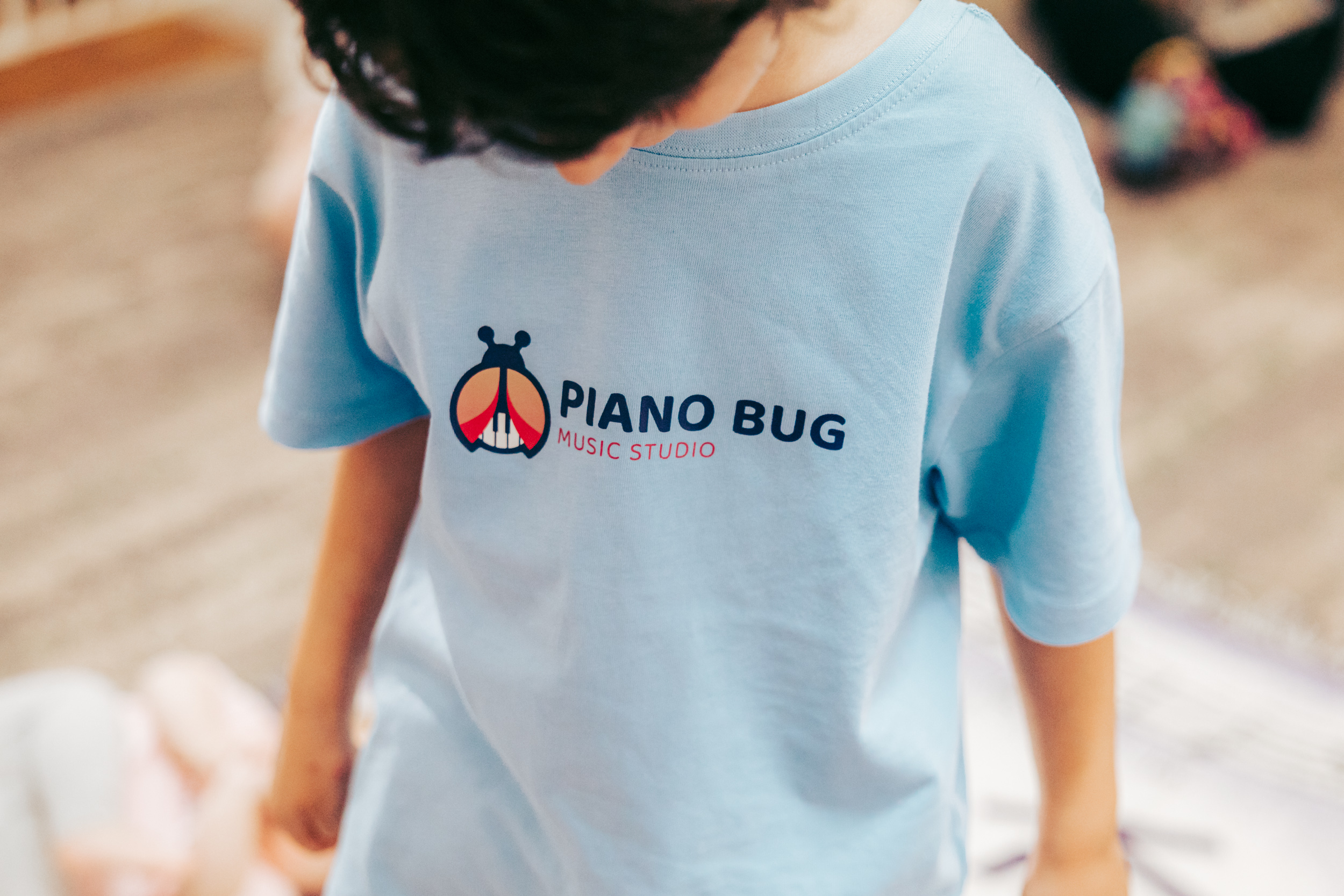 A young boy in a striped shirt presses piano keys with both hands, his face lit up with excitement, in a cozy, well-lit music room with colorful posters.