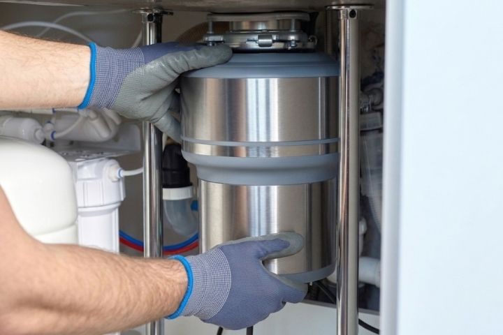 A plumber inspecting a kitchen unit to show how to unclog a garbage disposal.