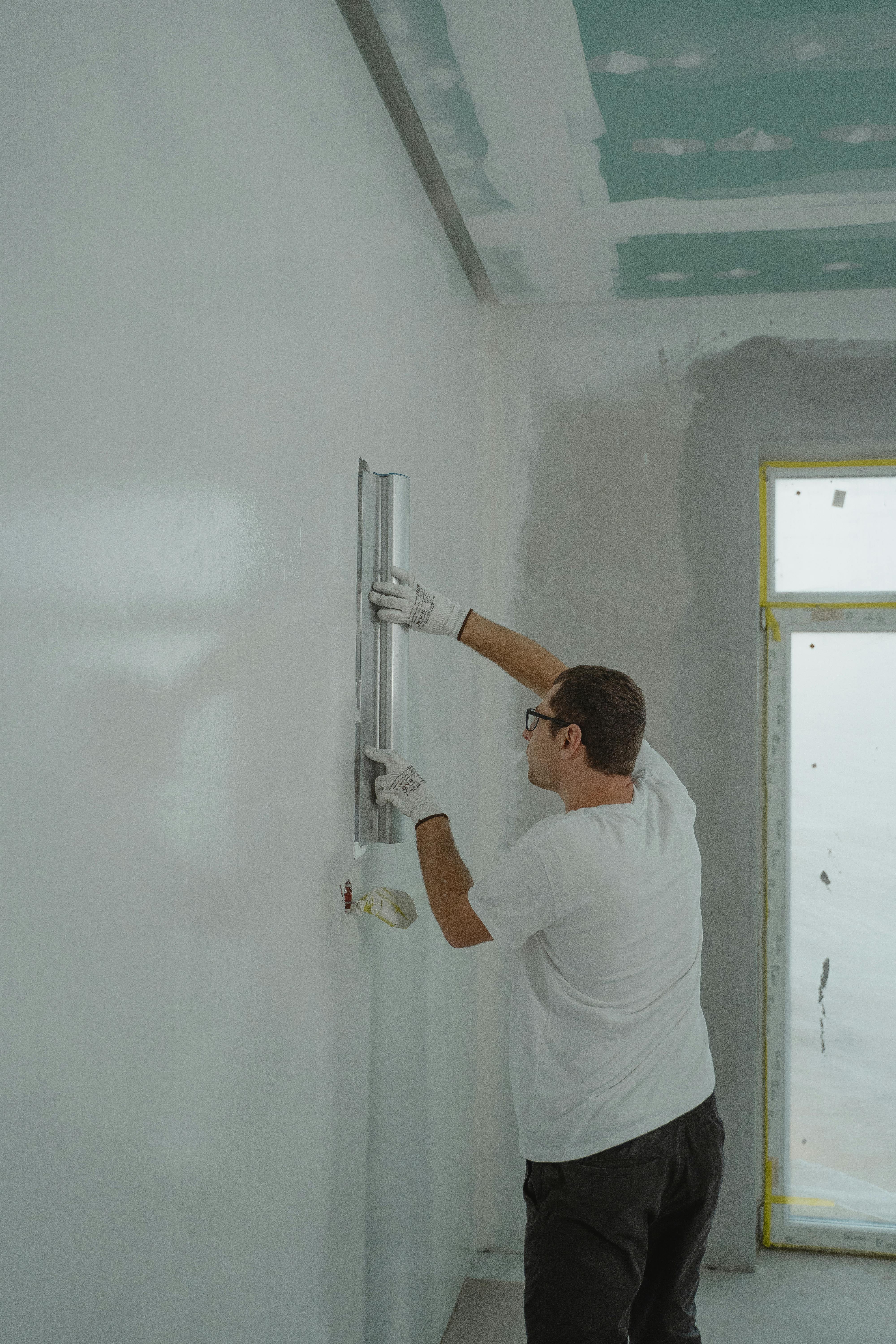 man using a metal slider to spread paint across wall