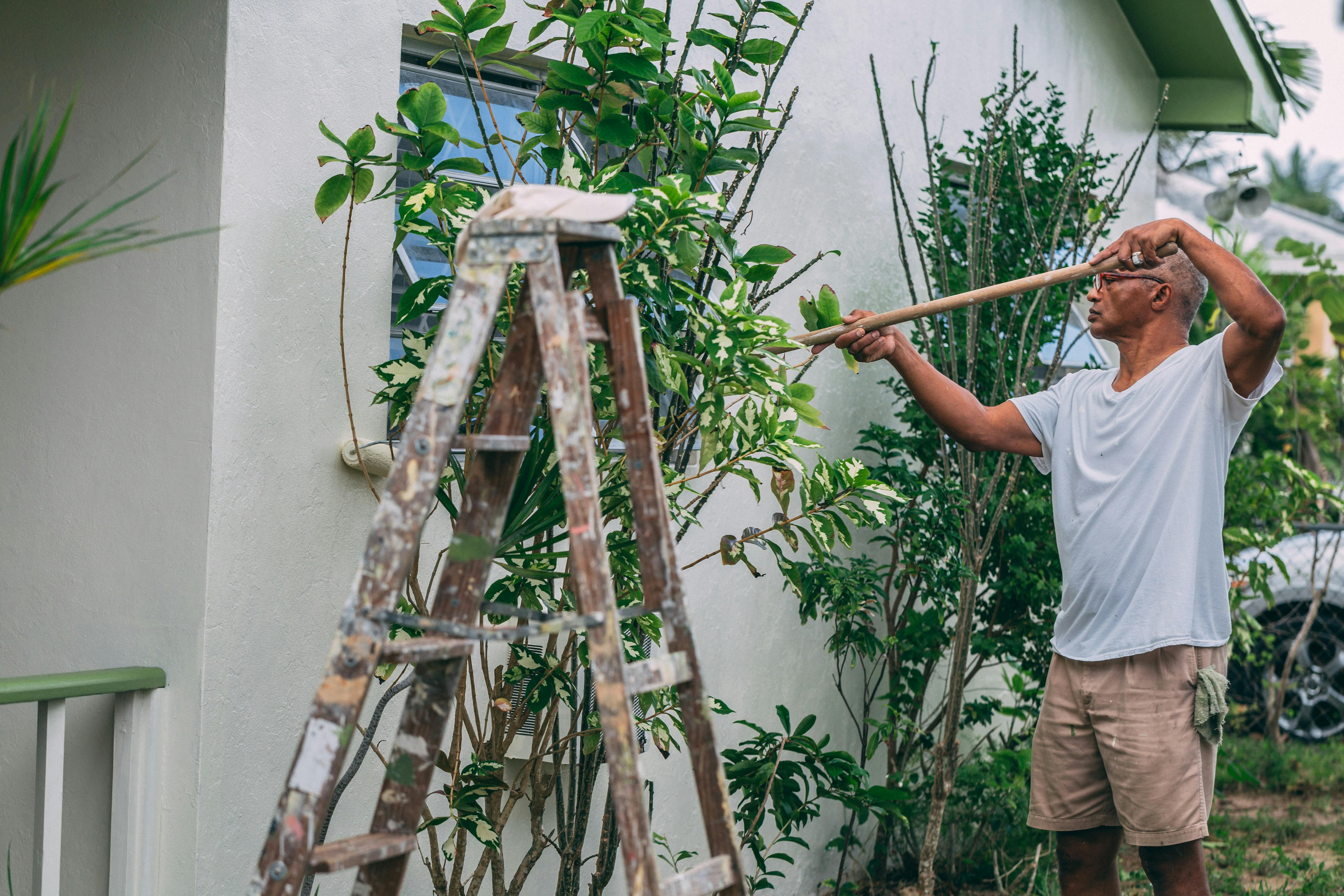 man in white tshirt and beige shorts paint wall of house