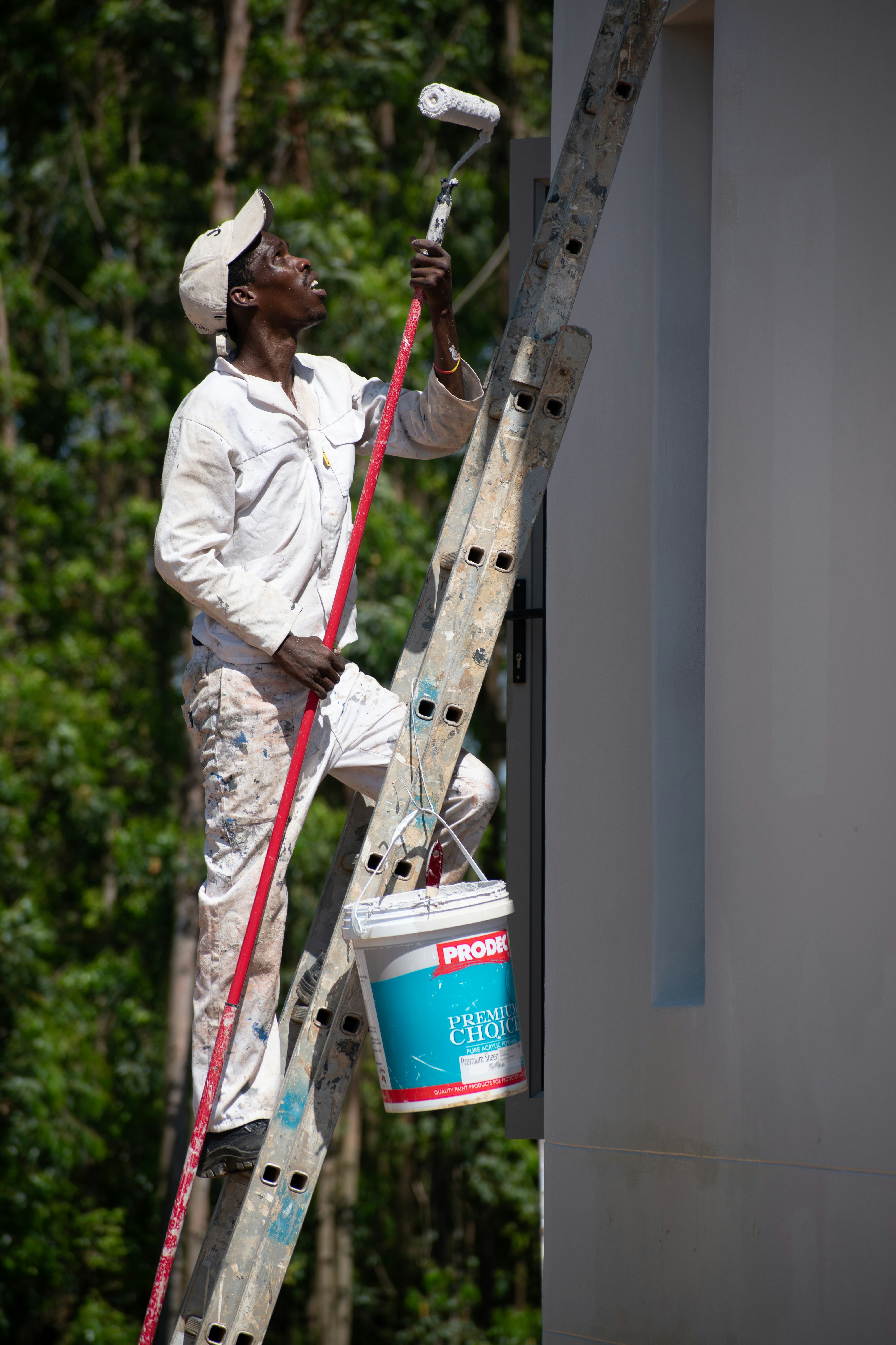 white shirt african man painting wall of house white using paint roller