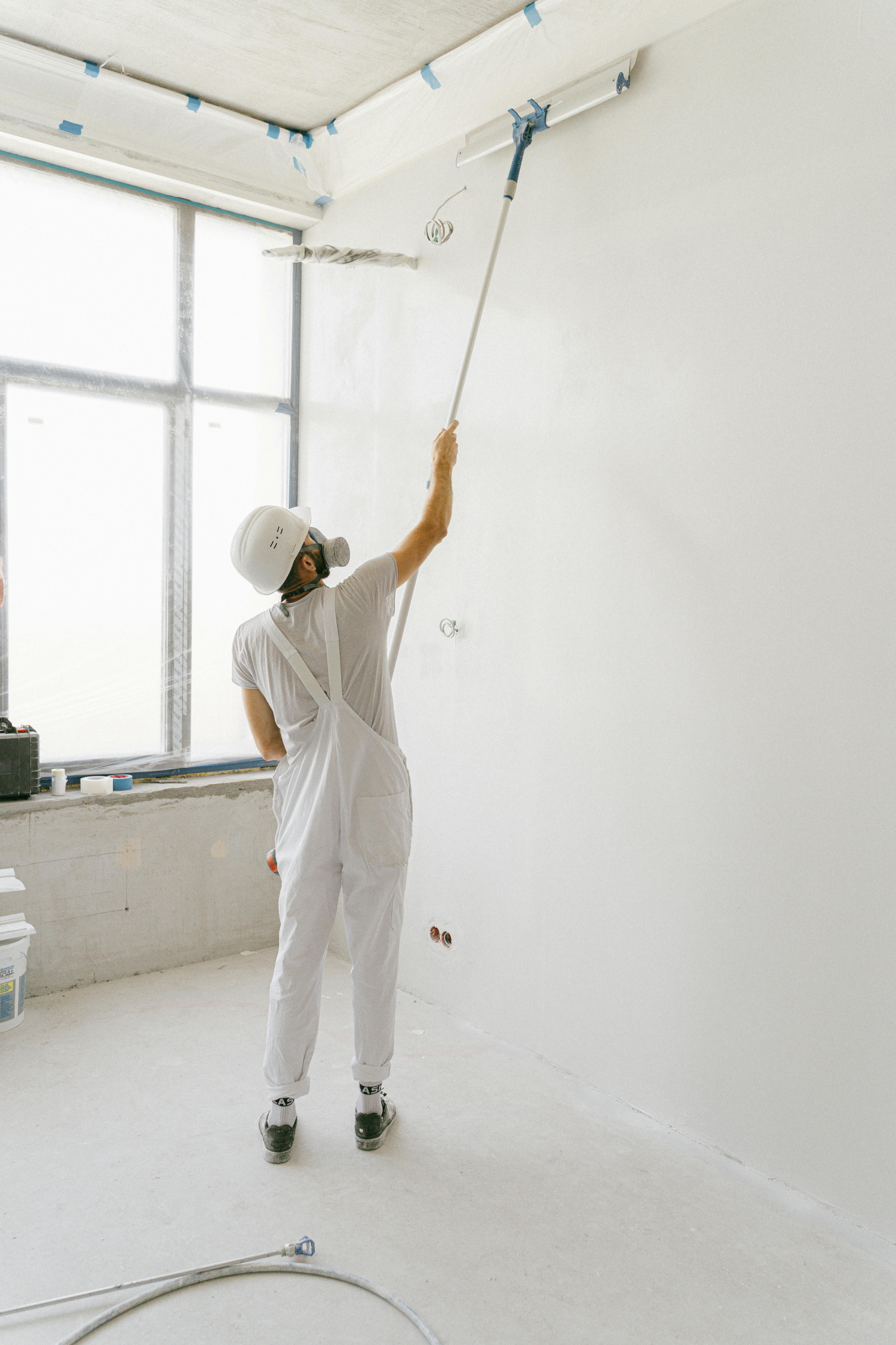 man using slider to spread white paint across wall
