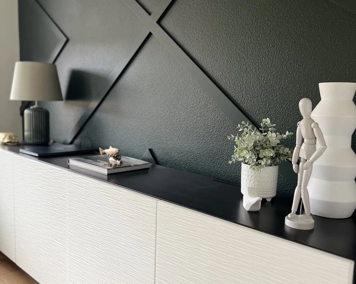Dark geometric accent wall with white textured credenza styled with sculptural décor and greenery