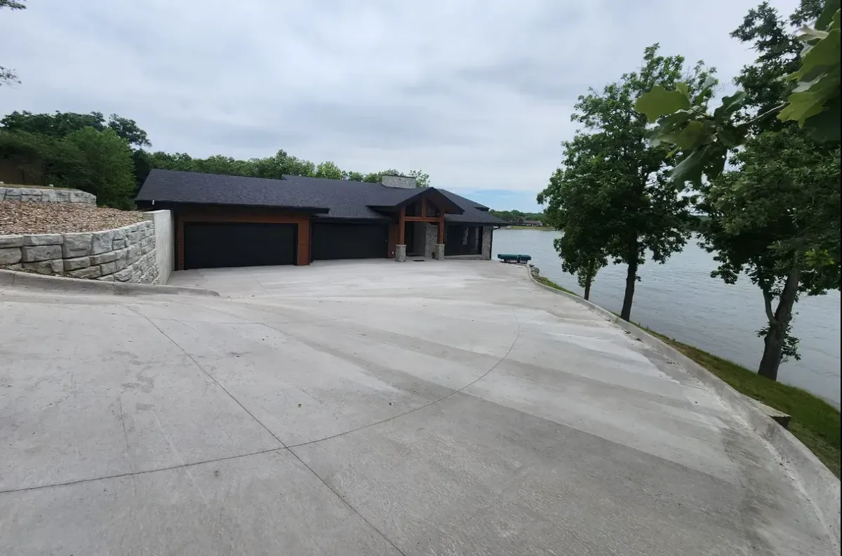 Large concrete driveway installation at lakefront home with stone retaining wall by Quick Concrete Solutions Iowa