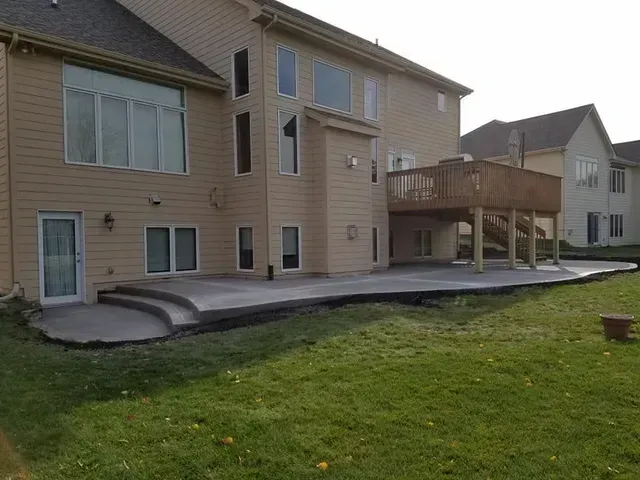 Large residential concrete patio with steps below elevated deck by Quick Concrete Solutions Iowa