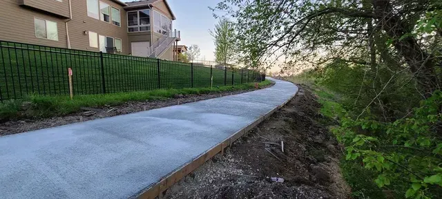 Curved concrete pathway installation along residential iron fence by Quick Concrete Solutions Iowa