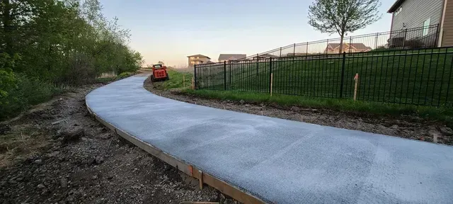 Freshly poured curved concrete walkway along iron fence at dusk by Quick Concrete Solutions Central Iowa