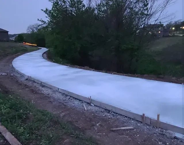 Freshly poured curved concrete driveway installation at dusk by Quick Concrete Solutions Central Iowa