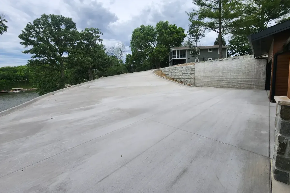 Sloped concrete driveway with stone retaining wall at lakefront home by Quick Concrete Solutions Iowa