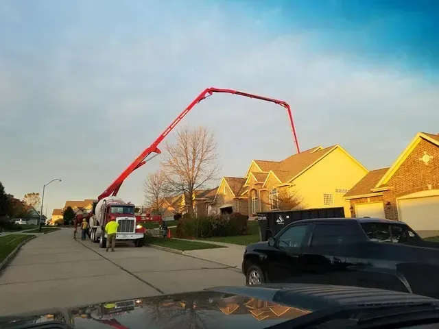 Concrete pump truck reaching over residential homes for driveway pour by Quick Concrete Solutions Iowa