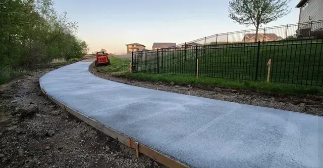 Curved concrete walkway installation along residential fence line by Quick Concrete Solutions Central Iowa