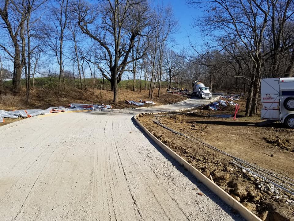 Winding concrete driveway installation through wooded rural property by Quick Concrete Solutions Iowa