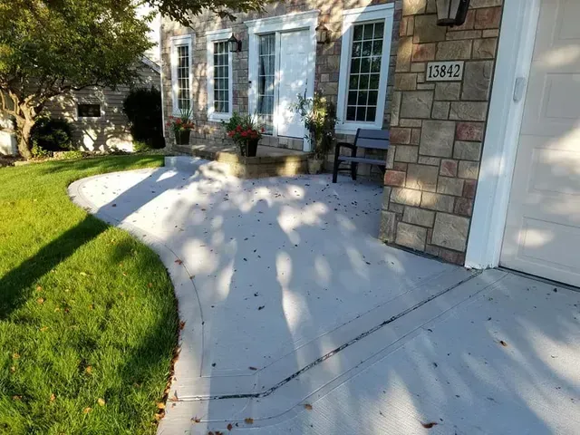 Curved concrete driveway and front walkway at stone exterior home by Quick Concrete Solutions Central Iowa