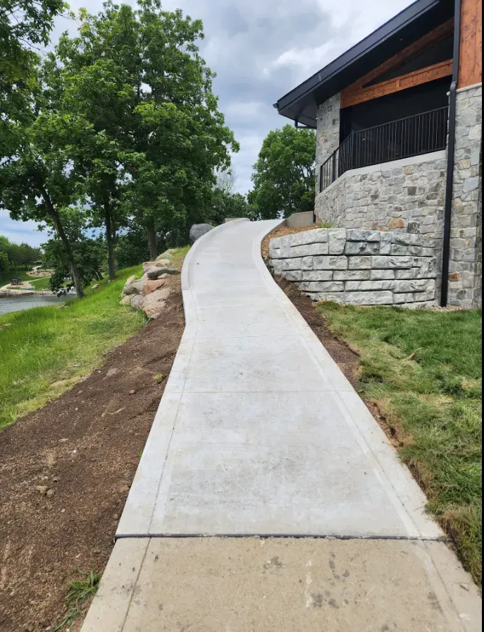 Curved concrete walkway installation along lakeside stone building by Quick Concrete Solutions Central Iowa