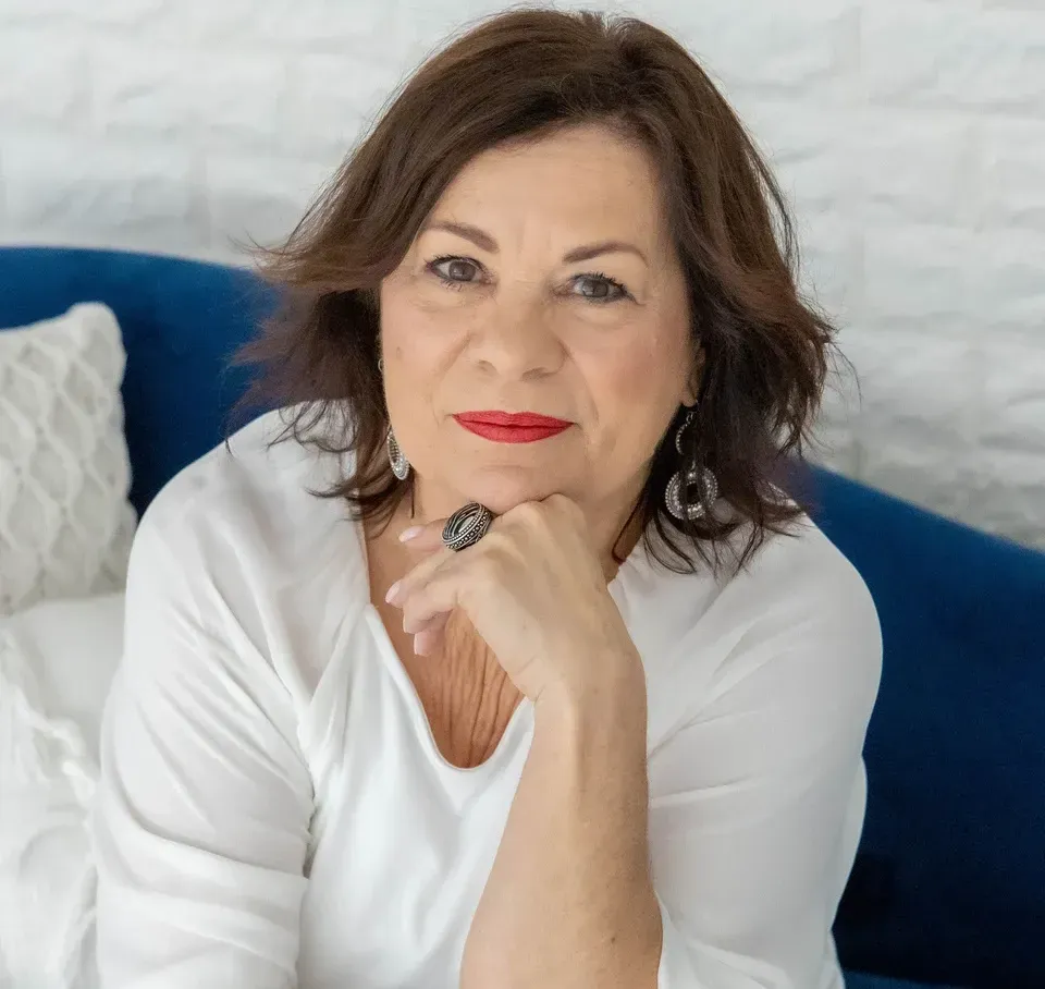 A woman sitting on a blue couch, looking thoughtful with her hand on her chin