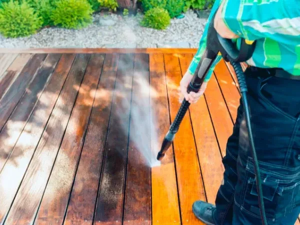 Professional cleaning a wooden deck with a pressure washer, showing bright wood contrast.”