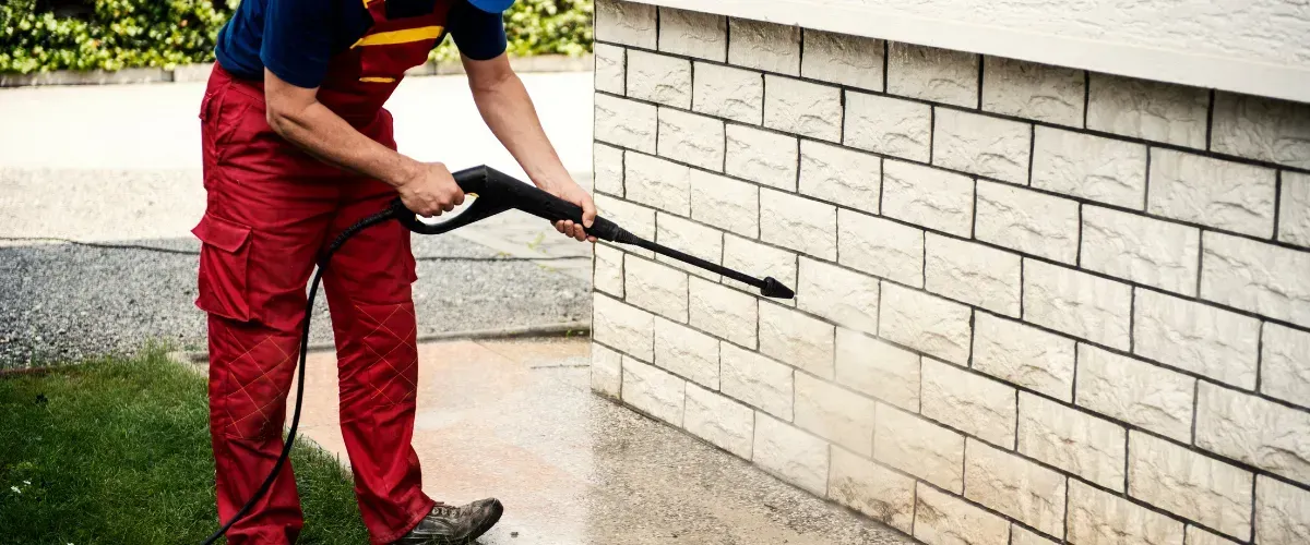 Worker using a pressure washer to clean dirt from the exterior wall of a house.