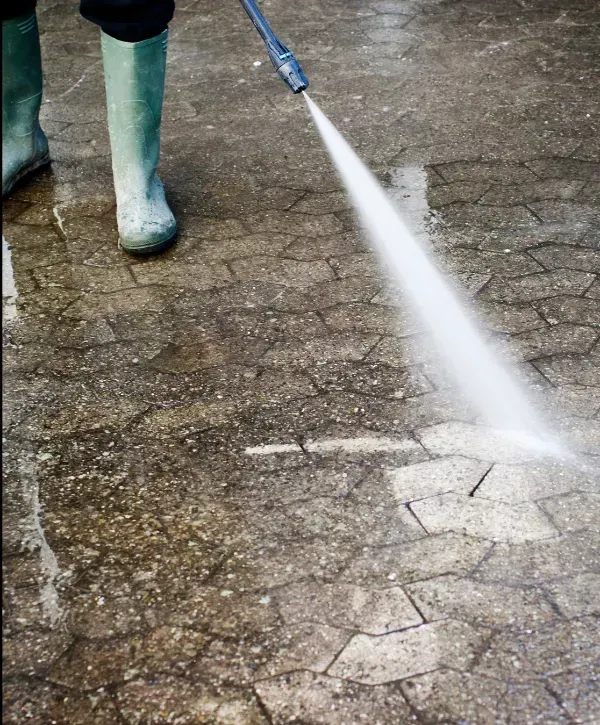 Worker using a high-pressure washer to clean dirt from a stone patio surface.