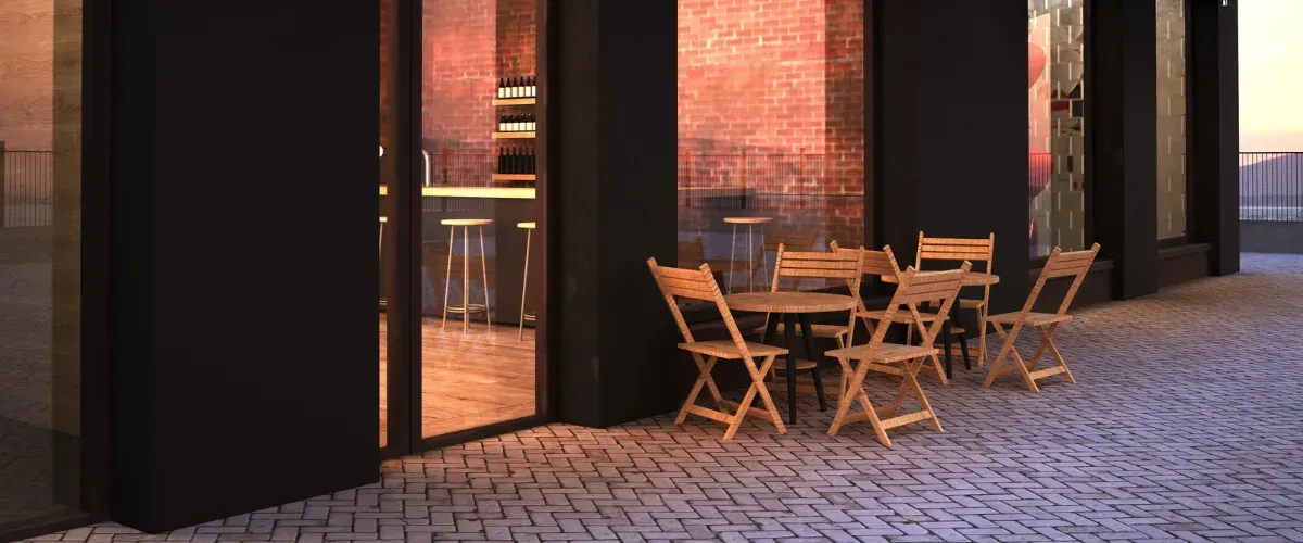 Outdoor café patio with wooden chairs and tables at sunset, next to a modern brick-and-glass storefront.