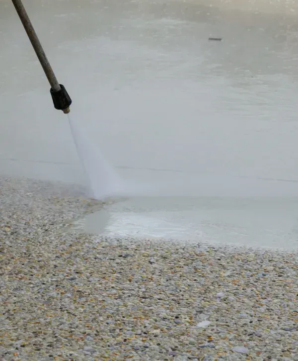 A power washer cleaning a gravel patio, with a stream of water blasting dirt and grime away from the surface.