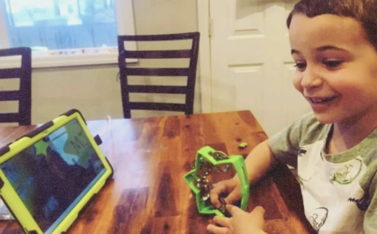 Boy holding a tambourine while watching the teacher on his tablet