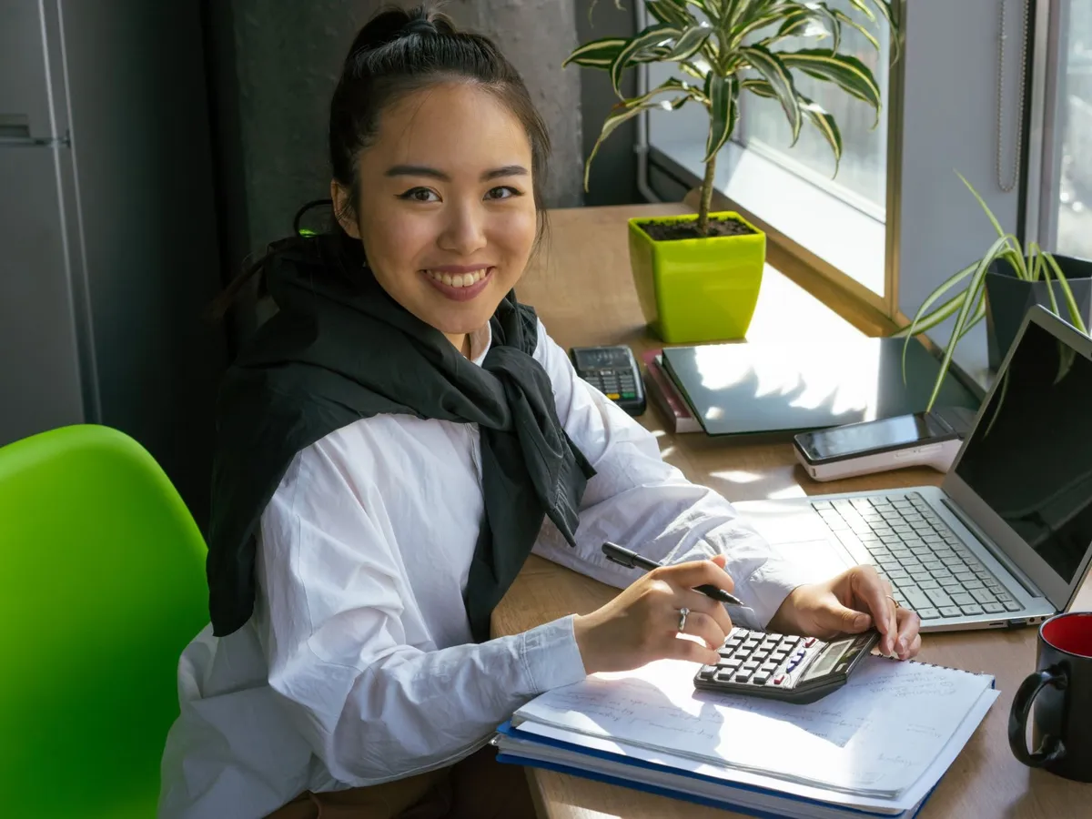 Young entrepreneur smiling while working through a budget with a calculator and notebook