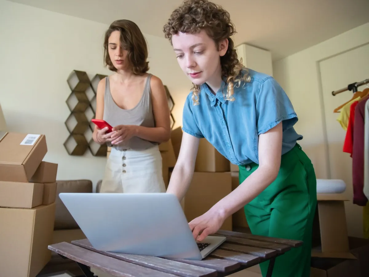Two young founders packing product orders and managing their online shop on a laptop