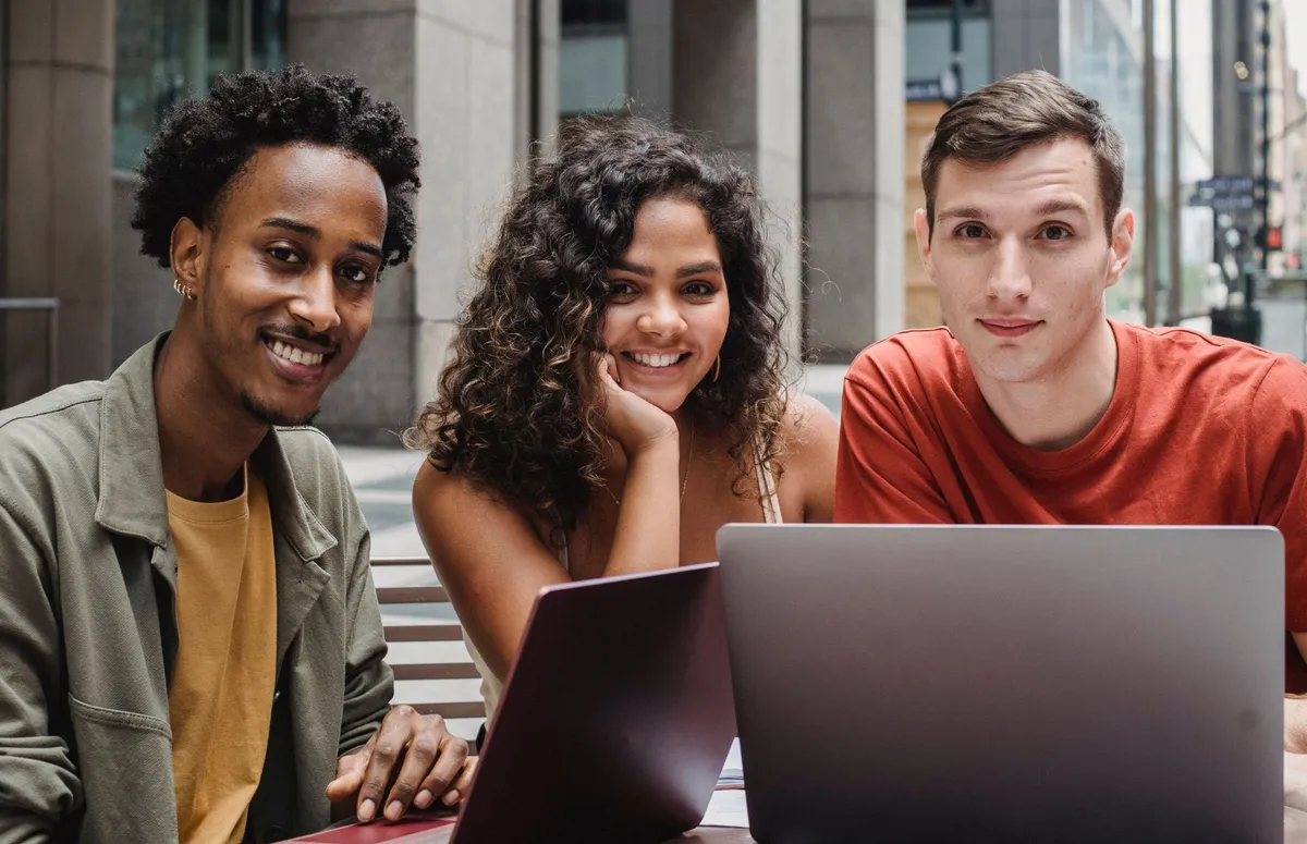 Three young founders smiling together while working on laptops
